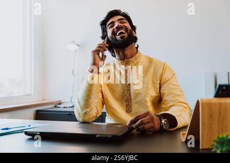 Un uomo d'affari pakistano in ufficio. Giovane uomo d'affari con abiti tradizionali che lavora nel suo ufficio. Venditore che effettua una telefonata con i clienti Foto Stock