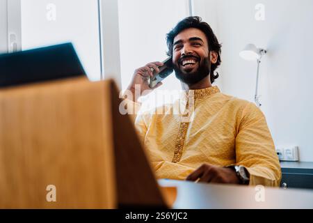 Un uomo d'affari pakistano in ufficio. Giovane uomo d'affari con abiti tradizionali che lavora nel suo ufficio. Venditore che effettua una telefonata con i clienti Foto Stock