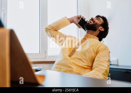 Un uomo d'affari pakistano in ufficio. Giovane uomo d'affari con abiti tradizionali che lavora nel suo ufficio. Venditore che effettua una telefonata con i clienti Foto Stock