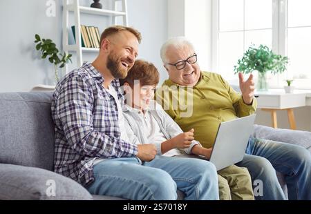 Una famiglia di uomini felice e multi-generazione seduti sul divano, che utilizzano il laptop insieme per l'intrattenimento online Foto Stock
