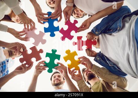 Vista dal basso di una gente felice sorridente che mette insieme pezzi di grandi puzzle di legno Foto Stock