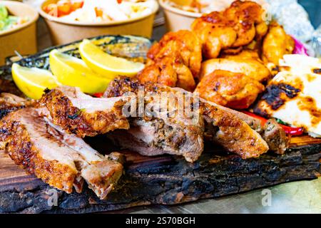 Un delizioso assortimento di carni alla griglia, spicchi di lime e vivaci contorni è esposto su un piatto di legno in un raduno all'aperto durante un sole Foto Stock