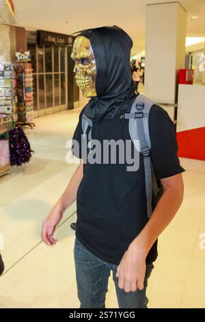 Un giovane con una felpa nera e una maschera si trova in un negozio. Indossa uno zaino e ha una maschera di scheletro sul viso Foto Stock