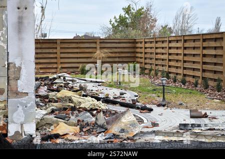 Danni causati da un incendio devastante che ha distrutto una casa privata. Resti carbonizzati e bruciati di un edificio danneggiato da un incendio con detriti sparsi nel cortile Foto Stock