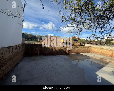 Escavatore parcheggiato in cima alle fondamenta di un edificio da costruire - il terreno è stato rimosso a diversi metri dal suolo e c'è cemento Foto Stock
