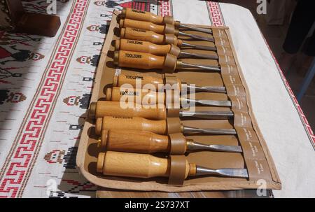 Primo piano di una serie di utensili per la lavorazione del legno utilizzati per riparare o creare oggetti in legno - scalpelli sparsi su una tovaglia in tessuto cretese su un tavolo all'esterno Foto Stock