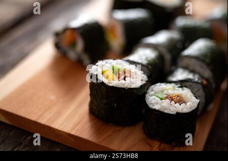 Primo piano di sushi ben disposti, ripieni di verdure e riso, posti su una tavola di legno, pronti per essere serviti. Foto Stock