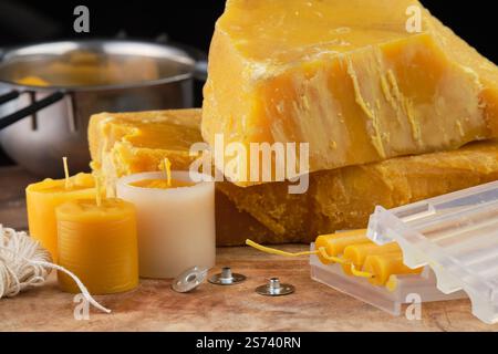 Cera d'api naturale, stampi, stoppini, stoppini metallici, melting pot, coltello e utensili per realizzare candele naturali fatte a mano su una superficie rustica in legno. Foto Stock