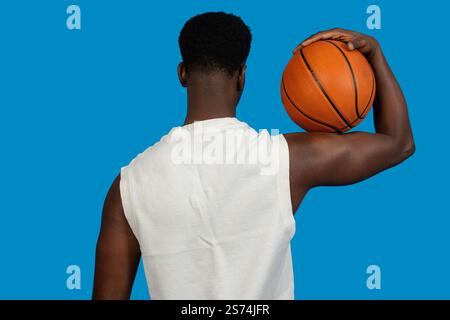 Vista posteriore di un giocatore di basket che tiene una palla sulla spalla, pronto all'azione su sfondo blu Foto Stock