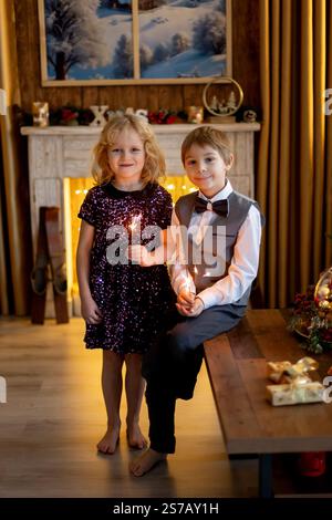 Fratello e sorella, bambini a natale, che tengono scintillanti davanti all'albero di Natale a casa Foto Stock