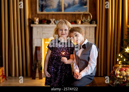 Fratello e sorella, bambini a natale, che tengono scintillanti davanti all'albero di Natale a casa Foto Stock