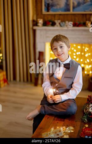 Bambino della scuola, ragazzo, in piedi a casa a natale, tenendo sparkler davanti all'albero di Natale, Natale Foto Stock