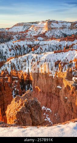 Una splendida vista del Parco Nazionale del Bryce Canyon con i suoi vivaci hoodoos arancioni spolverati di neve, circondati da paesaggi aspri e lontane innevate Foto Stock