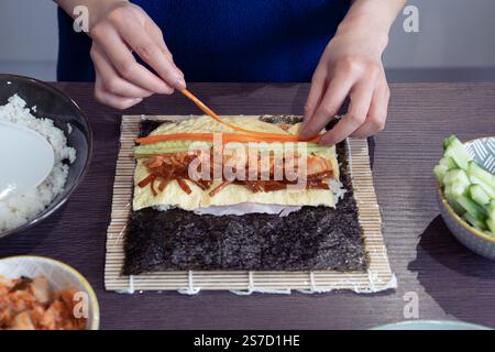 Donna asiatica che prepara il ripieno di verdure per Kimchi Gimbap - un popolare piatto sudcoreano con un impacco nori (alghe commestibili) e riso sushi. REGNO UNITO Foto Stock