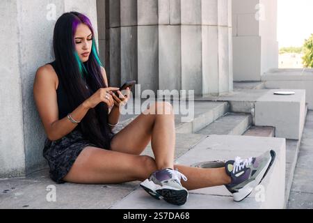 Giovane donna seduta con il suo cellulare su un atterraggio per scale Foto Stock