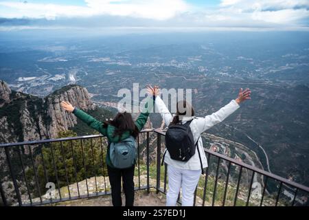 Due donne viaggiatrici alzano le braccia sulla cima di una montagna con il vasto paesaggio sullo sfondo. Foto Stock