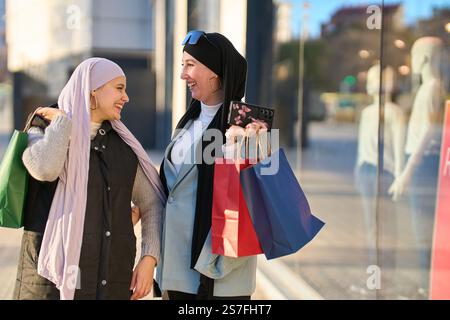 Due donne musulmane che trasportano borse della spesa camminano e parlano di fronte a un negozio Foto Stock