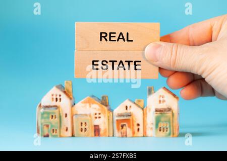 Case in miniatura e blocchi di legno con le parole Real Estate tenute in mano ad un agente immobiliare. Parole concettuali. Mercato immobiliare. Bell'hotel Foto Stock