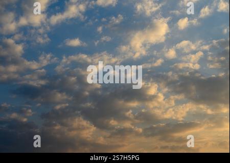 I colori si fondono al tramonto, proiettando un caldo bagliore su soffici nuvole che si spostano tranquillamente sopra l'orizzonte. Foto Stock