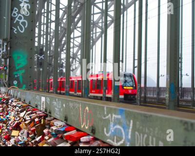 Un treno regionale in direzione della stazione centrale di Colonia, Köln Hauptbahnhof (Hbf) sulla Hohenzollernbrücke, con i famigerati lucchetti d'amore visti sulla t Foto Stock