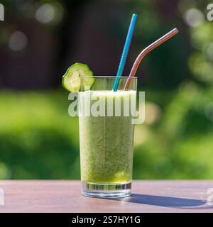 Bicchiere di frullato verde sul tavolo di legno nel Cafe' sullo sfondo naturale, da vicino. Sana bevanda biologica a base di banana, aneto, prezzemolo, cetriolo A. Foto Stock