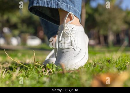 Una persona cammina con cautela su un'erba verde lussureggiante indossando scarpe da ginnastica bianche. Foto Stock