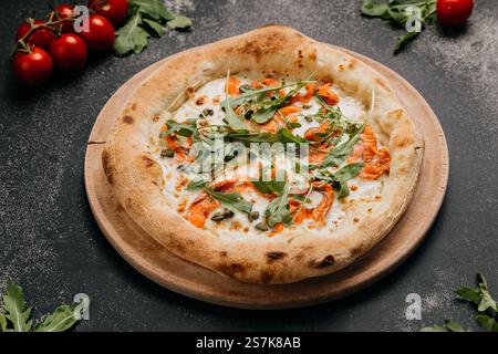 Pizza gourmet con salmone affumicato, rucola, capperi e formaggio fuso su un piatto di legno Foto Stock