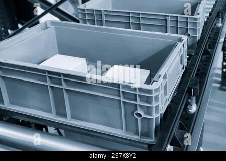Due contenitori in plastica grigia su un nastro trasportatore. I contenitori sono vuoti e sono in attesa di essere riempiti Foto Stock