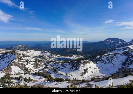 Paesaggio maestoso caratterizzato da una catena montuosa innevata con un lago tranquillo in una valle lontana sotto un cielo estivo limpido e blu Foto Stock