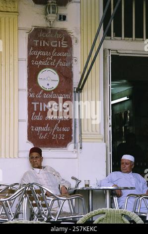 Due più anziani gentiluomini marocchini vestiti con abiti religiosi siedono su un tavolo in un bar che si guarda intorno e bevono tè a Tangeri, in Marocco. Foto Stock