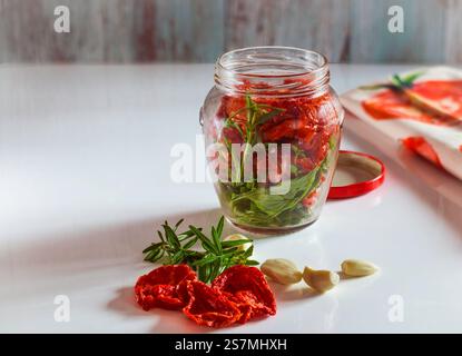 Pomodori secchi con rosmarino fresco e aglio in un vaso di vetro, Solanum lycopersicum. Foto Stock