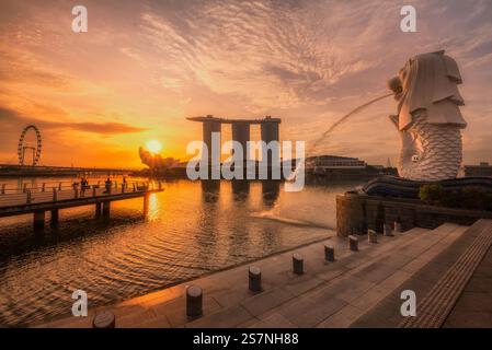 La splendida vista dell'alba su Marina Bay mostra l'iconica statua del Merlion con lo skyline della città che si riflette nell'acqua, creando un'atmosfera serena. Foto Stock