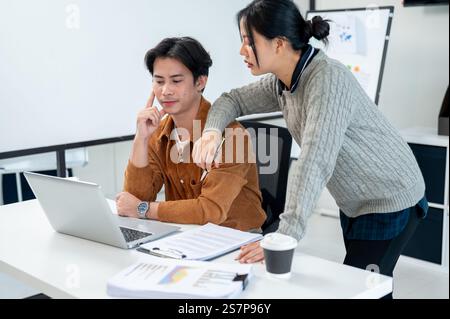 Due uomini d'affari asiatici, concentrati e seri, guardano lo schermo di un notebook, proponendo soluzioni di brainstorming per risolvere i problemi del loro progetto, lavorando insieme io Foto Stock