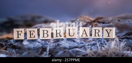Febbraio è una parola da vicino fatta di cubi di legno per bambini in natura, sullo sfondo di montagne blu. Febbraio è l'ultimo mese dell'inverno Foto Stock