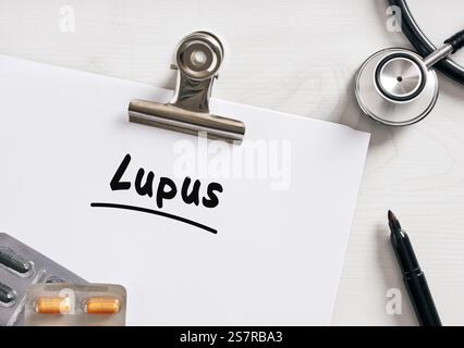 Rapporto medico che mostra la diagnosi del lupus, sdraiato sul tavolo accanto allo stetoscopio, pillole e pennarello, concetto sanitario Foto Stock