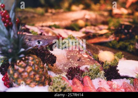 Una selezione di pesce fresco esposto con verdure e frutta in un mercato di pesce Foto Stock