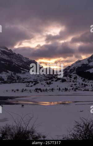 Tramonto invernale mozzafiato con colori vivaci che illuminano le vette innevate e un lago parzialmente ghiacciato nel Parque Montaña de Riaño, León, Spagna Foto Stock