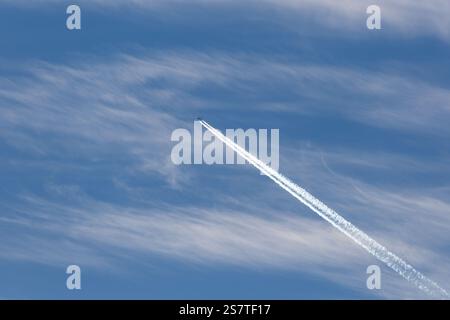 Un aereo a reazione lascia un contrale in un cielo blu con nuvole cirrus Foto Stock