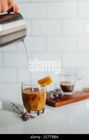 Il latte viene versato nel caffè con bordo di miele in una cucina bianca pulita Foto Stock