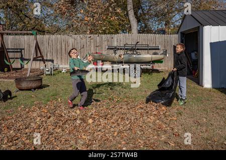 Due ragazzi che giocano con un mucchio di foglie in un cortile in una giornata di sole Foto Stock