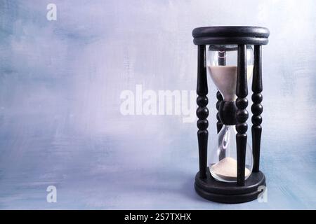 Timer sabbia in una cornice in legno nero con supporti decorativi su un BG blu-grigio Foto Stock