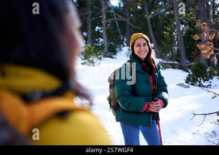 Ritratto di una donna latina che cammina guardando la macchina fotografica sorridendo, in piedi fuori in una foresta innevata. Foto Stock