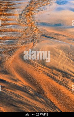 L'immagine mostra gli intricati schemi creati dal movimento dell'acqua sulla sabbia. L'acqua, riflettendo la luce, ha scolpito la sabbia. Foto Stock