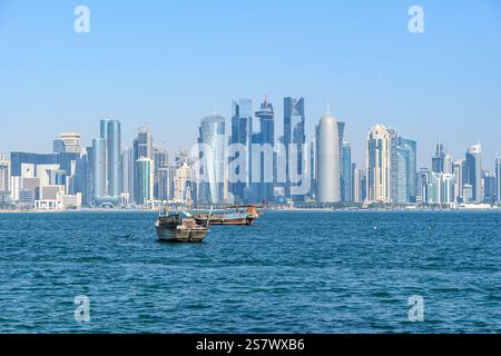 Doha, Qatar - 4 gennaio 2025: Il sole al tramonto proietta una tonalità dorata sulla città, mentre i dù tradizionali navigano nel Golfo Persico contro l'iconica Doha Foto Stock