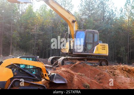 I macchinari pesanti operano in cantiere circondati da alberi, mostrando attività di movimento terra. Foto Stock