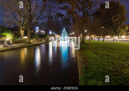 Albero di Natale illuminato in piedi nel fiume Windrush a Bourton on the Water, nella splendida Cotswolds, Inghilterra, Regno Unito. Dicembre 2024 Foto Stock