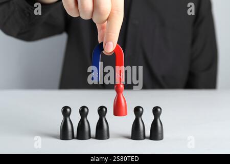Donna con magnete che attrae pezzi rossi tra quelli neri al tavolo bianco, primo piano Foto Stock