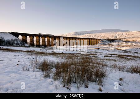 Un treno passeggeri attraversa il viadotto Ribblehead (noto anche come Batty Moss) in un giorno d'inverno, con la vetta Whernside sullo sfondo. Foto Stock