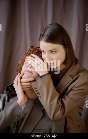 Ripresa verticale di una giovane donna adulta attraente che guarda dritto mentre chiude gli occhi di un uomo dai capelli ricci Foto Stock