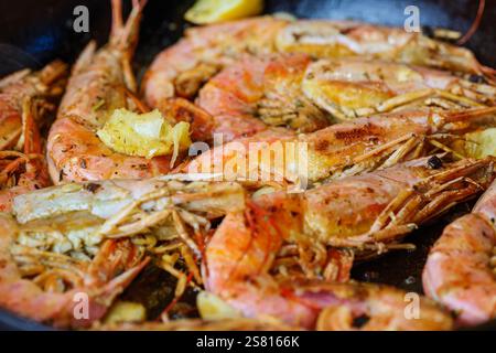 Cuocere il langoustine sulla padella con burro, limone e aglio. Gamberi grandi grigliati, longoustine cotti su una padella con spezie, erbe e limone. Foto Stock